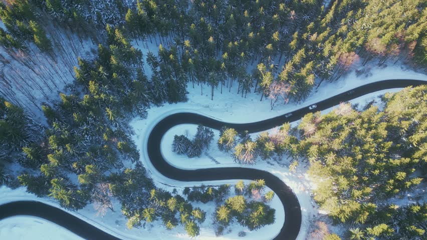 Twisted road in winter forest. Asphalt road serpentine and snowy landcape around. Aerial 4K footage from drone flight