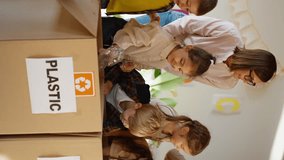 Vertical video of a woman teacher in a pink shirt with glasses with a bob hairstyle teaching them together with preschool children how to properly sort glass, plastic and paper in a special box in a