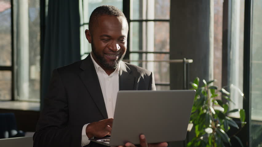Senior specialist 50s businessman stand with laptop in sunbeams office middle-aged African American male employer working online computer data analysis adult business man looking at camera happy smile | Shutterstock HD Video #1111954667