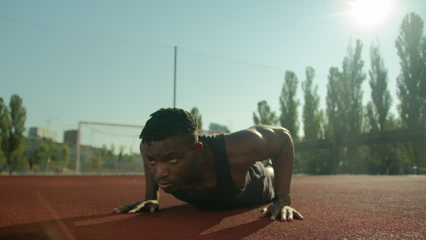 Motivated African American sport man athlete bodybuilder doing push ups exercise on football stadium male young sportsman fitness trainer in city training arms biceps muscles summer workout outdoors | Shutterstock HD Video #1111954679