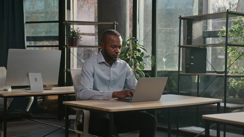 Professional middle-aged 40s ethnic African American business man senior businessman office employee sit indoors search net data on laptop computer networking looking at camera smiling positive smile | Shutterstock HD Video #1111954701