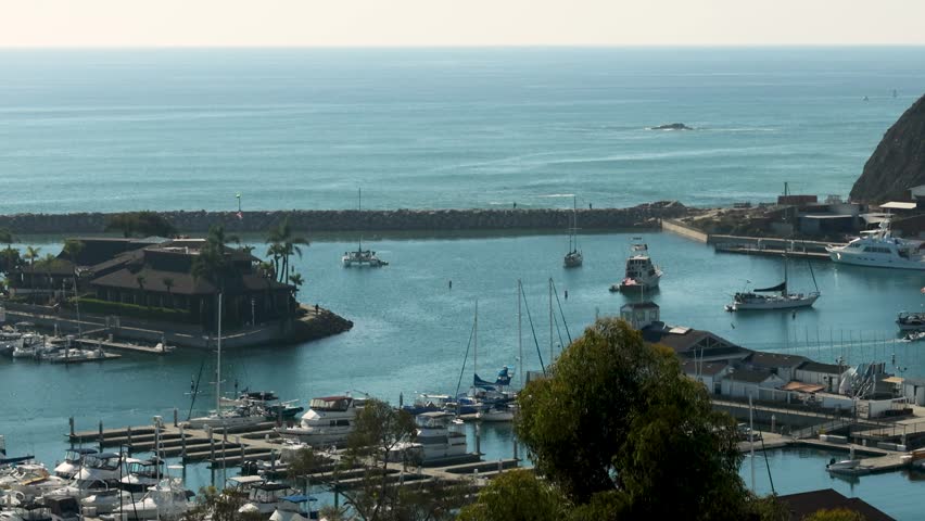 footage of the boats and yachts sailing in the Dana Point Harbor with vast blue ocean water and lush green trees and people on paddle boards at Dana Point Bluff Top Trail in Dana Point California USA Royalty-Free Stock Footage #1111955155