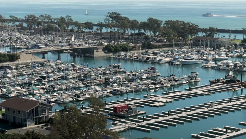 panning footage of the boats and yachts docked in the Dana Point Harbor with vast blue ocean water and lush green trees at Dana Point Bluff Top Trail in Dana Point California USA Royalty-Free Stock Footage #1111955165