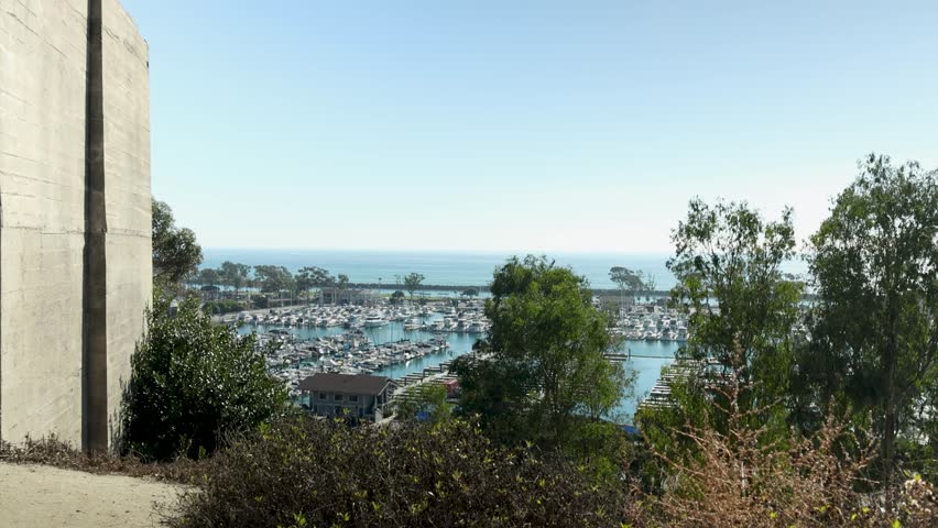 panning footage of the boats and yachts docked in the Dana Point Harbor with vast blue ocean water and lush green trees at Dana Point Bluff Top Trail in Dana Point California USA Royalty-Free Stock Footage #1111955173