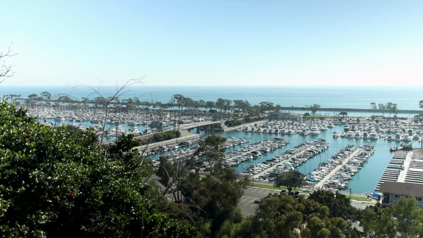 panning footage of the boats and yachts docked in the Dana Point Harbor with vast blue ocean water and lush green trees at Dana Point Bluff Top Trail in Dana Point California USA Royalty-Free Stock Footage #1111955187