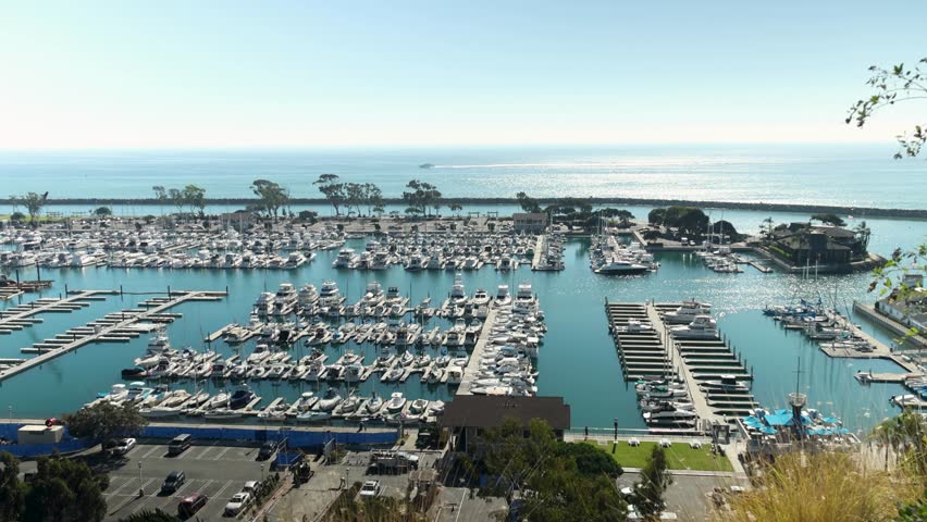panning footage of the boats and yachts docked in the Dana Point Harbor with vast blue ocean water and lush green trees at Dana Point Bluff Top Trail in Dana Point California USA Royalty-Free Stock Footage #1111955193