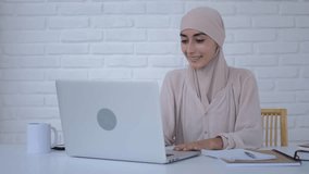 Muslim female psychologist in hijab at home of laptop and conducts online consultation with patient. Online psychotherapy session available from every part of globe. Concept of accessible online help
