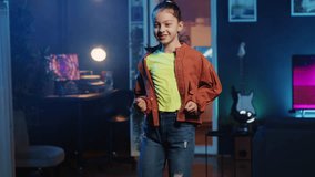 Happy kid dancing in dimly lit home studio interior, producing content for online channel. Talented girl doing viral dance choreography in apartment illuminated by RGB lights