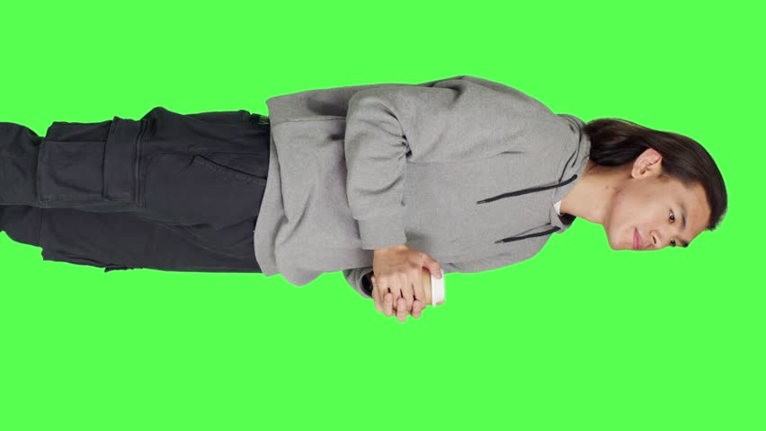 Side view of person drinking cup of coffee on camera while standing in front of greenscreen template, enjoying caffeine refreshment. Young asian man holding hot beverage and feeling pleased. | Shutterstock HD Video #1111955557