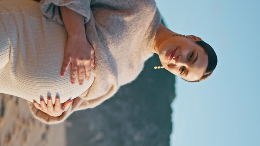 Pregnant girl posing seashore with happy smile vertically. Beautiful expectant mother looking camera on sand beach enjoying pregnancy. Dreamy woman expecting baby contemplating ocean waves at evening. Royalty-Free Stock Footage #1111956323