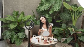 Beautiful content creator making natural beauty and cosmetic tutorial at green plant leave garden video. Beauty blogger showing how to apply beauty care to social medial audience. Blithe