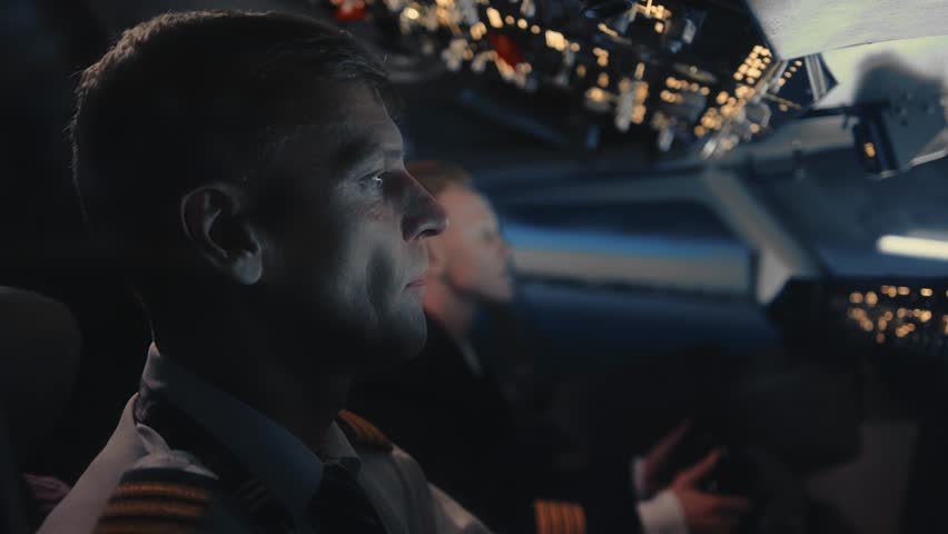Airplane Pilots in Plane Cockpit Flying at Night Time Sky Closeup. View on Professional Men Sitting in Aircraft and Using Technology to Flight Control Study. Aviator Face in Dark Scenic Cabin Close-Up