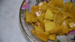 Pieces of mango served on a transparent plate with a floral pattern. Marble table. Panning Video 