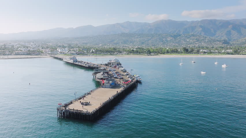 Aerial view of Stearns Wharf and Santa Barbara harbor with mountains, California, USA. Panoramic shot of old wooden pier-popular tourist attraction. Yachts and boats floating at of Pacific Ocean coast | Shutterstock HD Video #1111965765