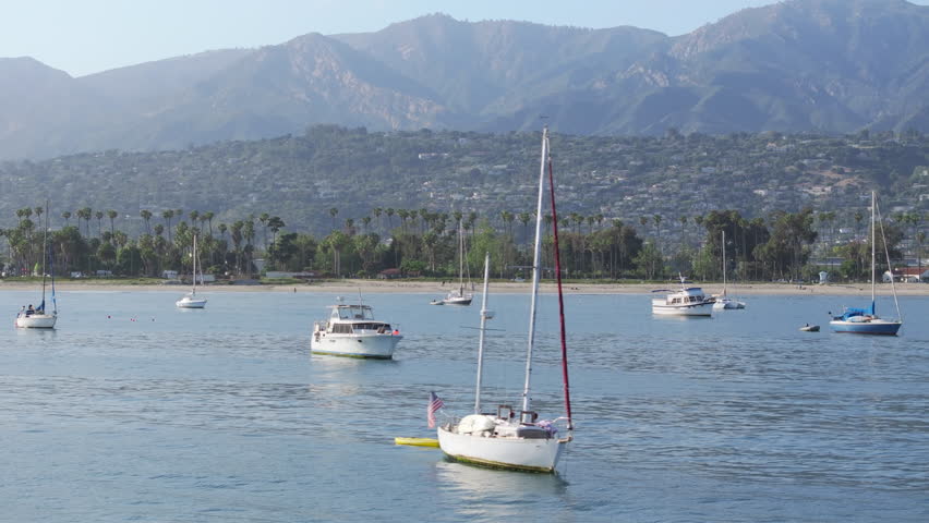 Scenic view of yachts floating in Santa Barbara Harbor, California, USA. Shot from Point Castillo on Santa Barbara city surrounded mountains and Pacific Ocean. Sailboats docked in city marina  | Shutterstock HD Video #1111965771