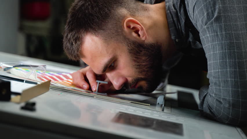Worker in a printing and press center uses a magnifying glass and check the print quality