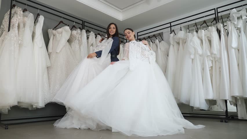 Portrait of two happy brides in a bridal salon with wedding dresses in their hands, they are enjoying a selection of dresses. Two women have chosen a wedding dress. Royalty-Free Stock Footage #1111972447