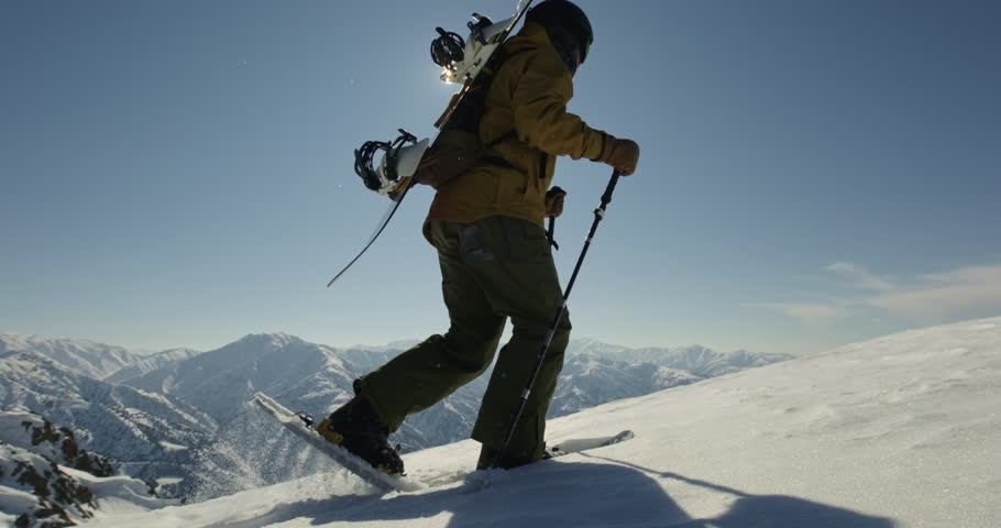 Freeride snowboarder conquering mountain peak to ride down pristine slope. Man with snowboard in snowshoes climb the mountain, extreme freeride snowboarding