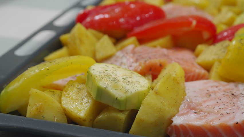 cooking baked fish with vegetables, preparing salmon fillet with potatoes and vegetables on tray for baking in oven
