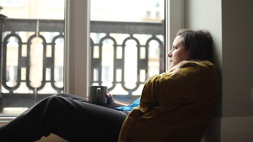 Middle-aged frustrated woman sitting on floor near window, covering face with hand, closing eyes, suffering from despair, holding grey cup. Depression, sorrow, hopelessness, psychological problems. | Shutterstock HD Video #1111982455