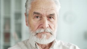 Close up portrait of a serious gray haired elderly man standing in living room at home. Handsome senior retired male posing looking at the camera. Headshot of confident thoughtful bearded pensioner - Powered by Shutterstock - Get 15% off with code: PIKWIZARD15