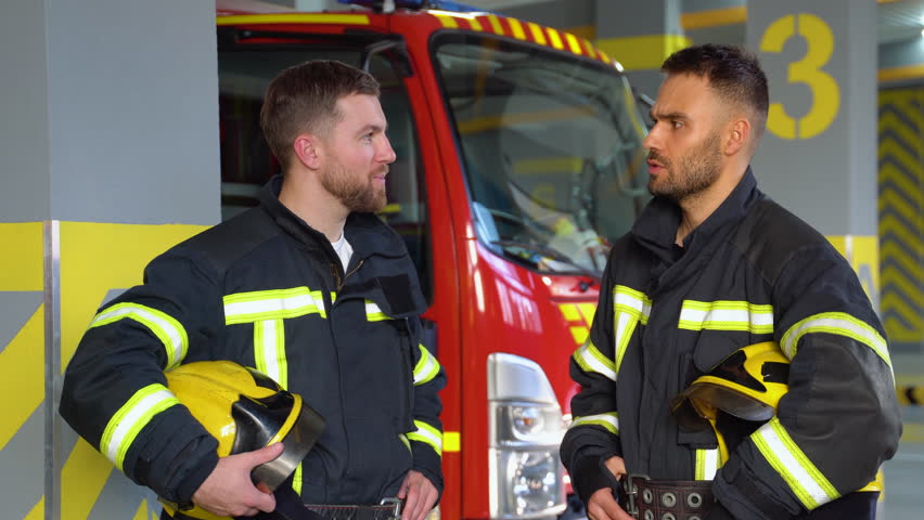 Two firefighters dressed in workwear with helmets in fire station | Shutterstock HD Video #1111982667