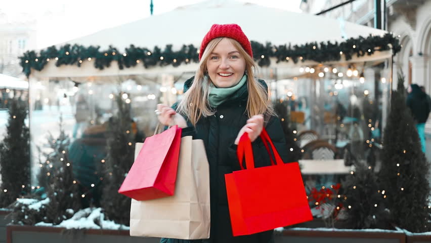 Attractive happy Caucasian blonde woman dancing with red present shopping bag at the Christmas market. Portrait of beautiful woman in snowy holiday Krakow city. High quality FullHD footage | Shutterstock HD Video #1111984927