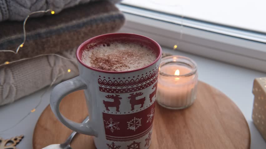 Winter windowsill still life. Red ceramic cup of hot coffee on window sill. Christmas decorations on the background. Cozy home picture. Warm woolen knitted sweaters, Burn Candle, Cookies. Stock photo | Shutterstock HD Video #1111986763