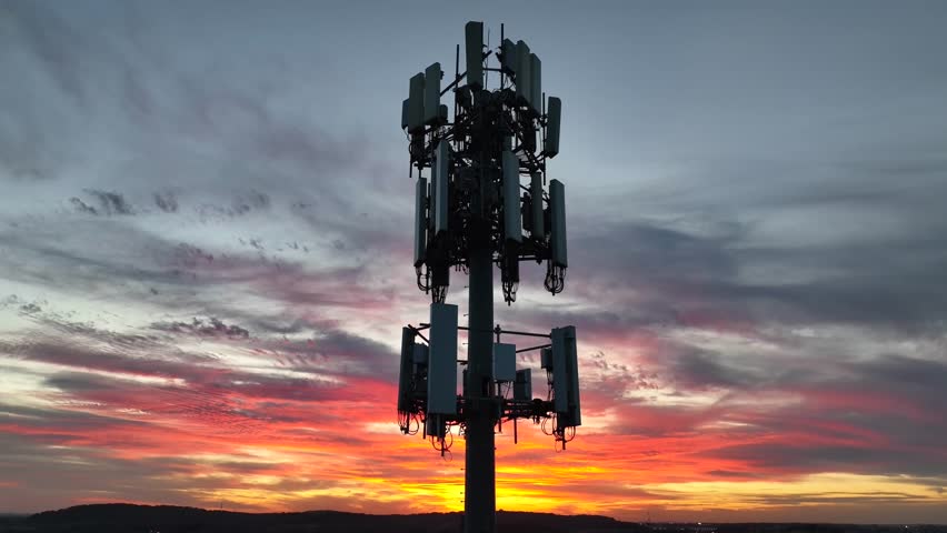 Cell phone tower at night against bright sunset sky in America. Communication and 5G internet speed. Cellular signal strength concept. Aerial. Royalty-Free Stock Footage #1111989071