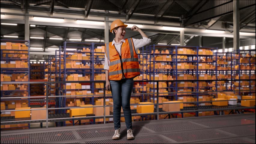 Full Body Of Asian Female Engineer With Safety Helmet Standing In The Warehouse With Shelves Full Of Delivery Goods. Flexing Her Bicep And Smiling To Camera In The Storage | Shutterstock HD Video #1111989373