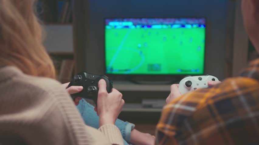 Couple of Gamers Playing Video Game on TV Screen with Console Controllers Close-up. Happy Man and Woman Have Fun at Home with Black and White Player Controls of PC. Two People Focused on Football 4k | Shutterstock HD Video #1111990501