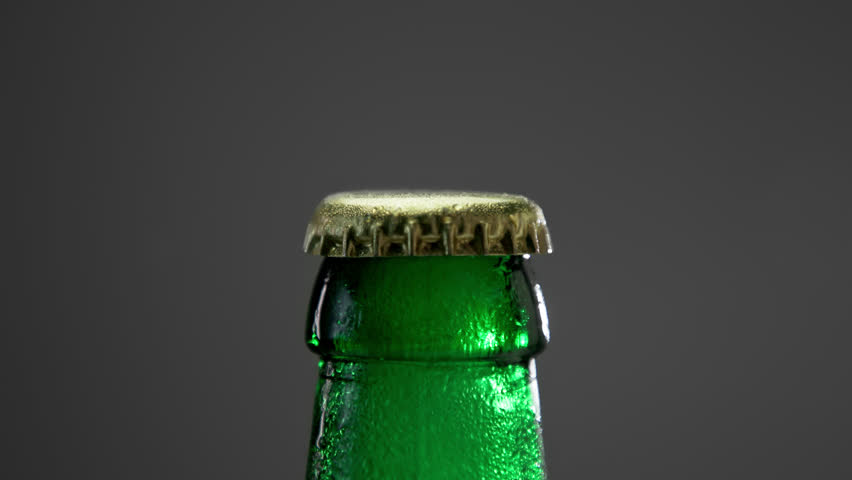 Cap of Full Beer Bottle Opens with Froth Smoke Closeup. Drinking Alcohol Beverage in Modern Bar or Dark Pub to Quench Thirst. Aluminum Lid Top and Colorful Glass in Wet Condensation on Grey Background | Shutterstock HD Video #1111990503