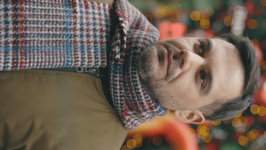 Vertical Video. Cheerful Gentleman Stands in Festively Adorned Town, Wrapped in Scarf, on New Year's Eve. Handsome Guy Standing Outdoors, Looking at Camera Smiling on Backdrop of Christmas Decorations | Shutterstock HD Video #1111992203