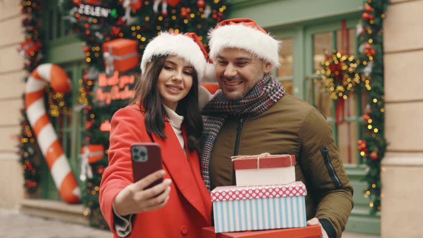 Happy Cheerful Married Couple Taking a Selfie on Grimacing at the Camera Outside. Two Friends Take Strange Photos on Their Phones Standing on the Decorated Street. People and Technology Concept | Shutterstock HD Video #1111992209