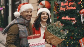 Two Friends Walking Together from the Christmas Shop with Gifts and Bouquet of Fir Trees. Happy Couple Going Home Before New Year Eve, Talking, Laughing together. Family and holiday Concept - Powered by Shutterstock - Get 15% off with code: PIKWIZARD15