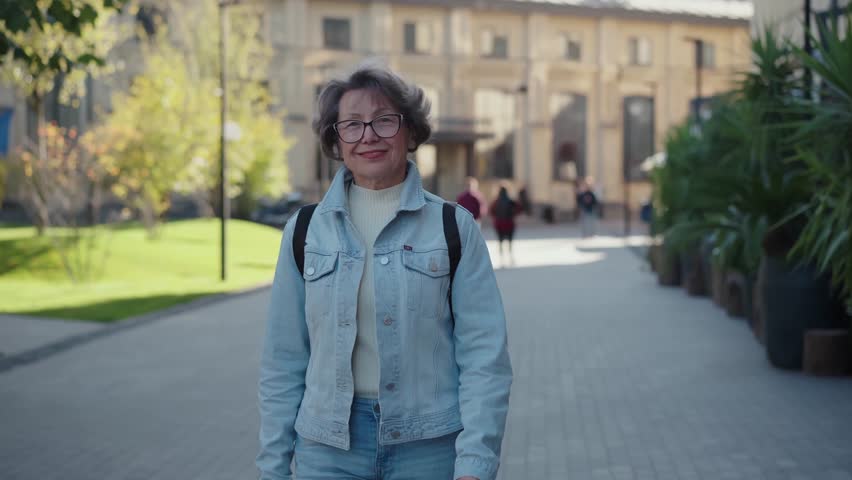Strolling disctricts alone. Elderly woman in motion exploring new city. Pensioner lady wear denim shirt strolling and looking at architecture details in city center. Positive old female tourist at | Shutterstock HD Video #1111993765