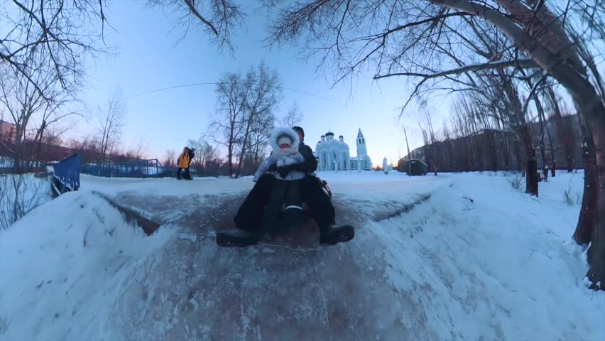 A little girl and her dad roll on a tube from a snow slide, a girl on a tube in winter