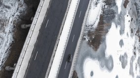 Vertical video. Drone snowy road. Aerial winter traffic. Countryside frozen lake with asphalted ice bridge surface cloudy day.