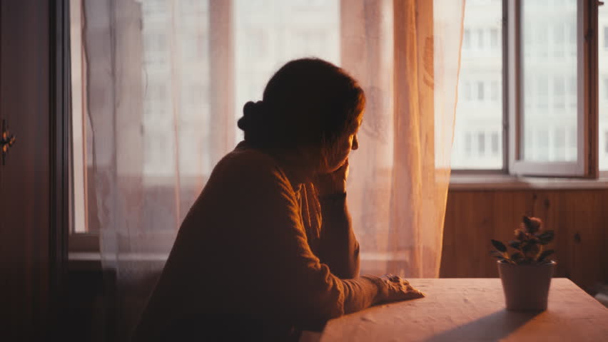 Sad grandmother sitting at table and looking out the window at sunset, nostalgia | Shutterstock HD Video #1111994755