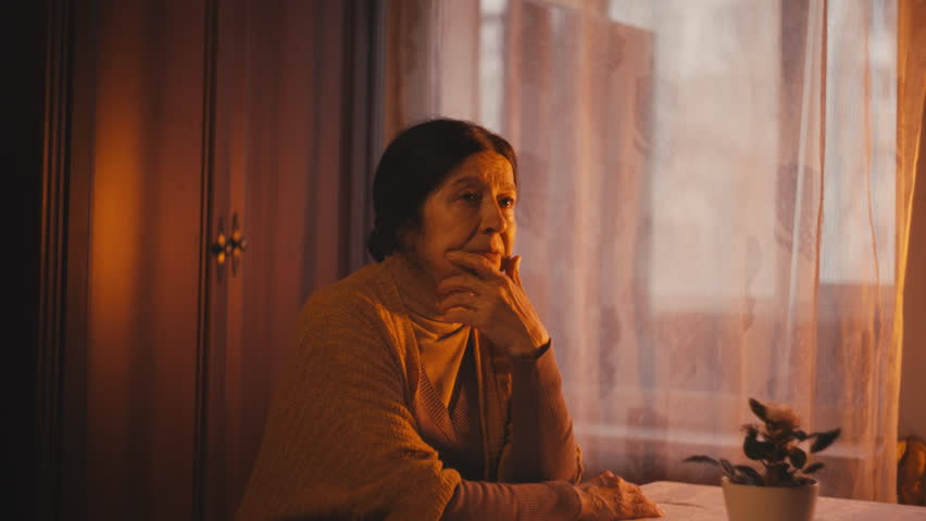 Unhappy woman in her 60s sitting alone at the table and looking out the window | Shutterstock HD Video #1111994759