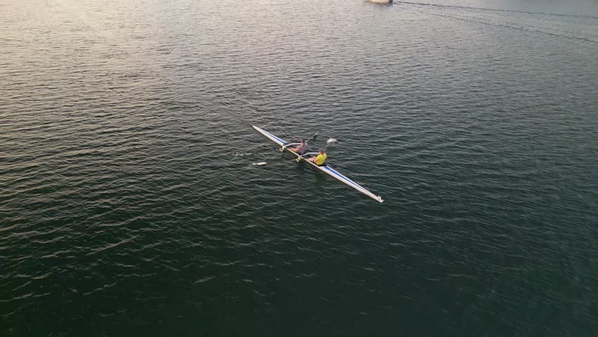 Team rowing on calm ocean water early in the morning Aerial view. A women's rowing team rows in an ocean bay at sunrise. Sport canoe driven by a team of two women practicing early in the morning.