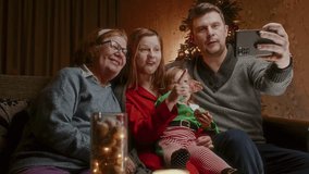 A family with a toddler and grandmother on Christmas Eve got a conference call with relatives, conversation by video call. Cozy apartment with Christmas decorations and a happy family.