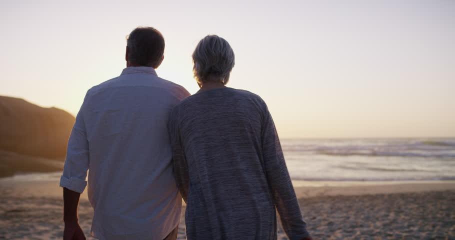 Happy couple, walking on beach and hand holding in sunset and married on holiday, outdoor and retired. Retirement, elderly or love for commitment, bonding together or care for romantic relationship