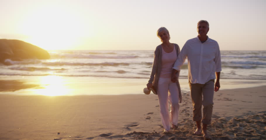 Couple, walking on beach and hand holding in evening and married on holiday, outdoor and retired. Retirement, elderly or love for commitment, bonding together or care for romantic relationship