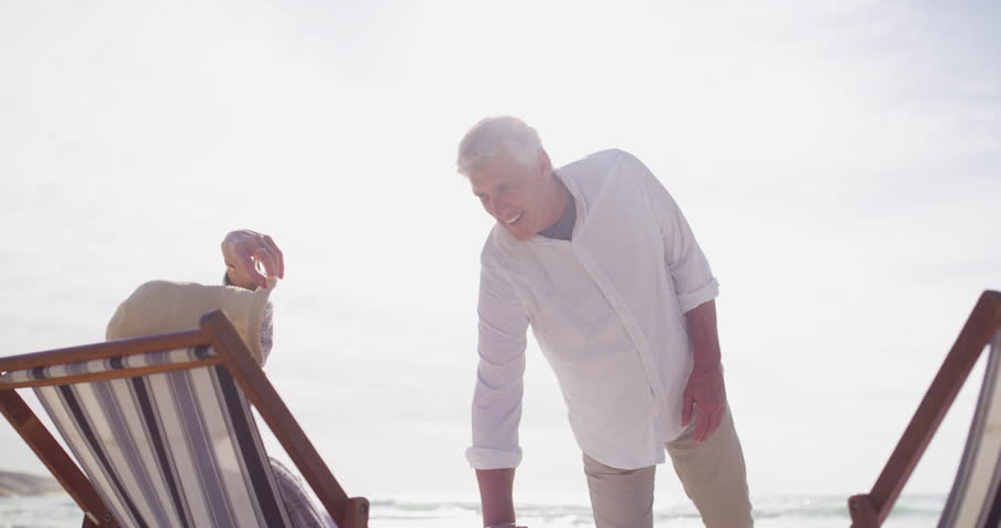 Senior couple, happy and holding hands on beach chair for care support, talking and relax on holiday. Mature man, woman and sunlounger for bond in marriage, love and vacation on retirement by seaside Royalty-Free Stock Footage #1112002901