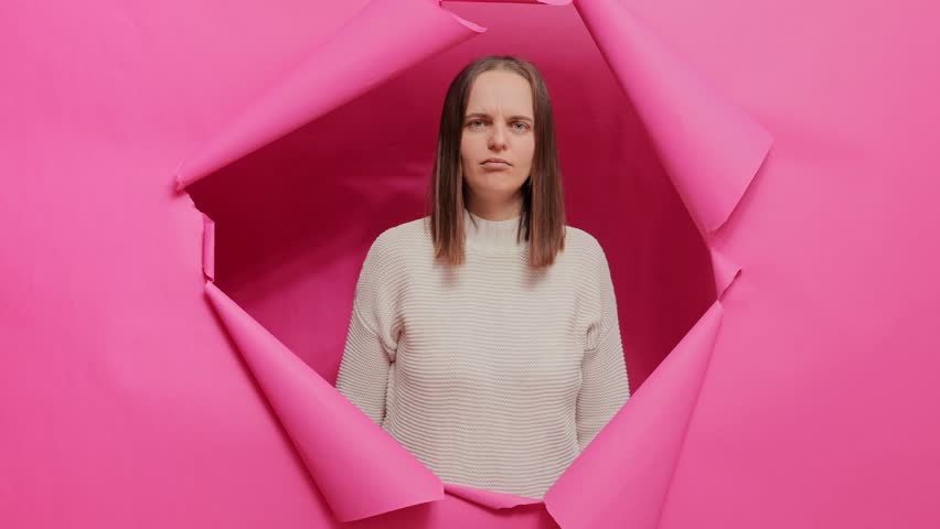 Worried sad brown haired woman wearing sweater posing through hole of pink paper wall making facepalm gesture bad memory forgot something important. | Shutterstock HD Video #1112003549