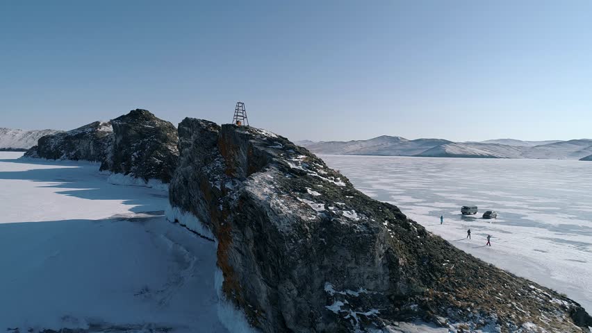 Aerial over the rocky cliff at lake Baikal. Winter landscape of frozen Baikal. Tourist walking around the cliff. Popular tourist spot