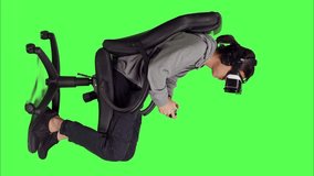 Profile of man engages in internet gameplay clash with friends while playing video games using mobile devices against greenscreen backdrop. With virtual reality glasses, person looks confident.