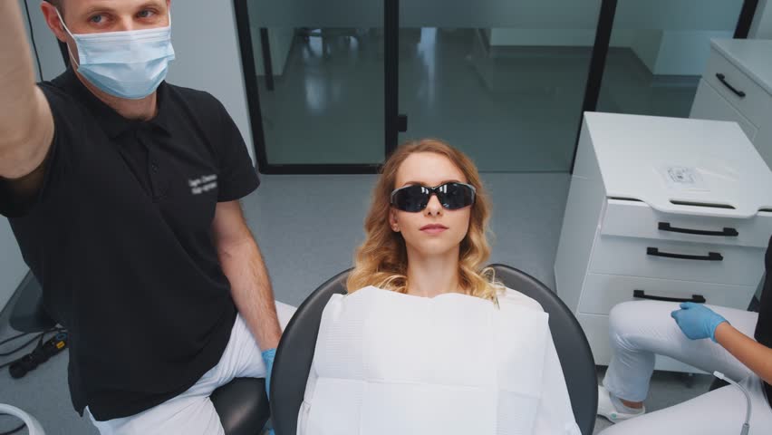In stomatology clinic patient wears protective glasses lying in dentist chair. Orthodontist doctor with assistant getting prepared for correcting teeth. Mouth hygiene. Dentistry. | Shutterstock HD Video #1112014939