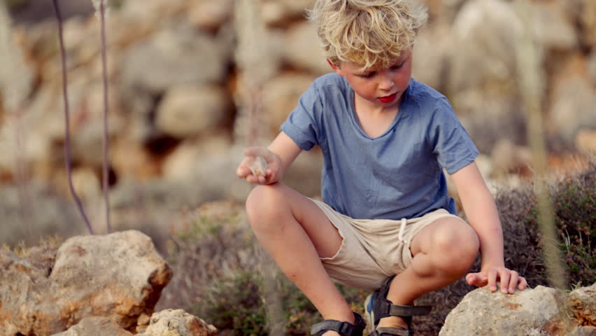 A young boy crouching with a stone in hand, tapping it into a larger rock | Shutterstock HD Video #1112016693